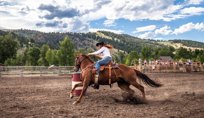 female barrel racing on a horse in a dirt pasture in the mountains